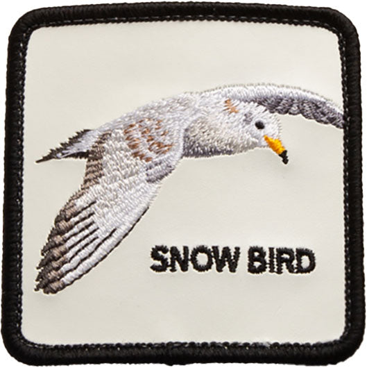 Weißes eckiges Cap-Logo mit schwarzem Rand, Stickerei einer fliegenden Möwe in Grau- und Brauntönen und schwarzer Schrift.